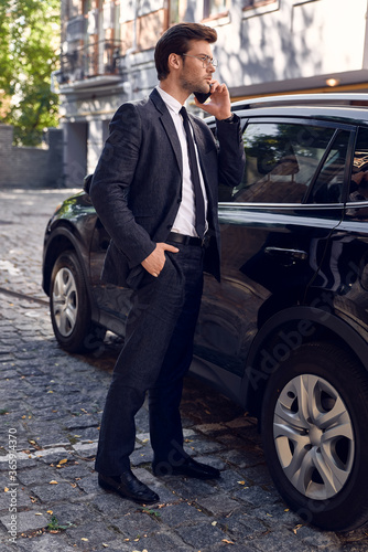 Confident business expert. Full length of handsome young businessman talking on the phone while standing near his car outdoors