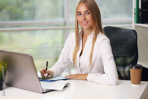 young beautiful businesswoman working on laptop in bright modern office, looking out the window