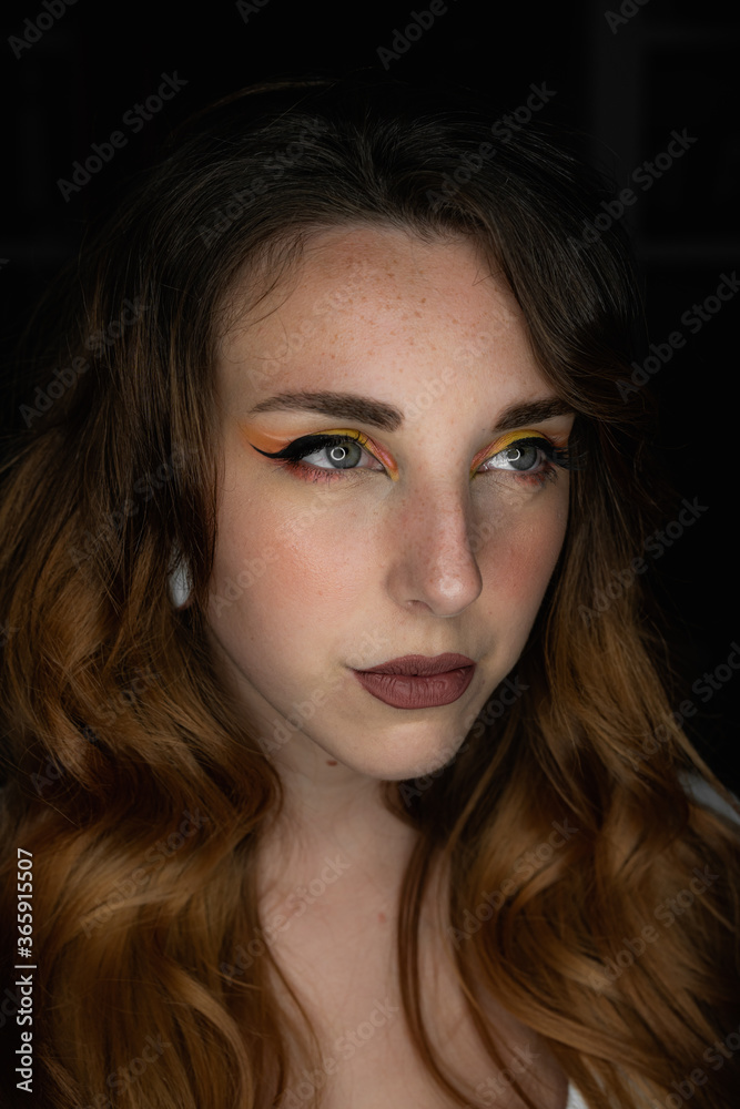 Modelo de maquillaje amarillo, naranja, negro y blanco, de ojos azules, pelirroja sobre fondo oscuro Modelo de maquillaje amarillo, naranja, negro y blanco, de ojos azules, pelirroja sobre fondo oscuro