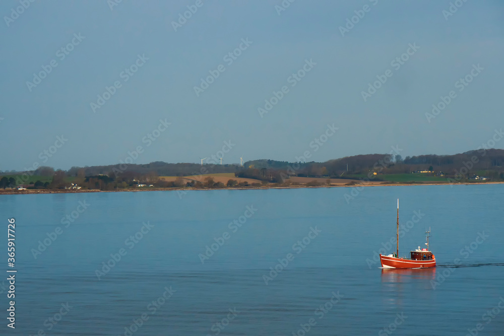 Red boat on the background of the shore with wind turbines, denmark coast, summer calm day, calm sea