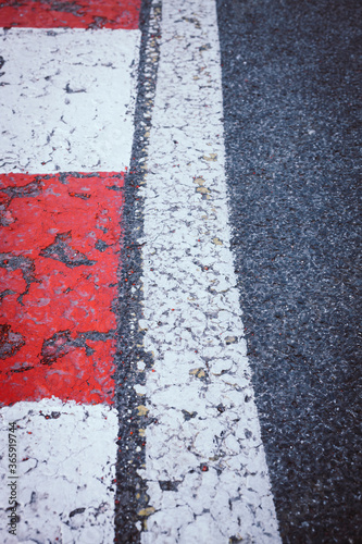 A white line on the left side of asphalt road with red and white painted curbs on the edge. Road turn traffic lines, race course road marking vertical background concept.