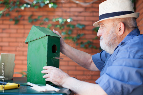 Fotografie, Obraz elderly man assembling a birdhouse