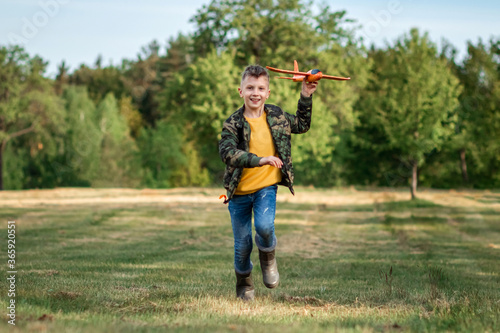 A boy runs across the field and launches a toy airplane against the backdrop of greenery. The concept of dreams, choice of profession, pilot, childhood. Copy space. © Aliaksandr Marko