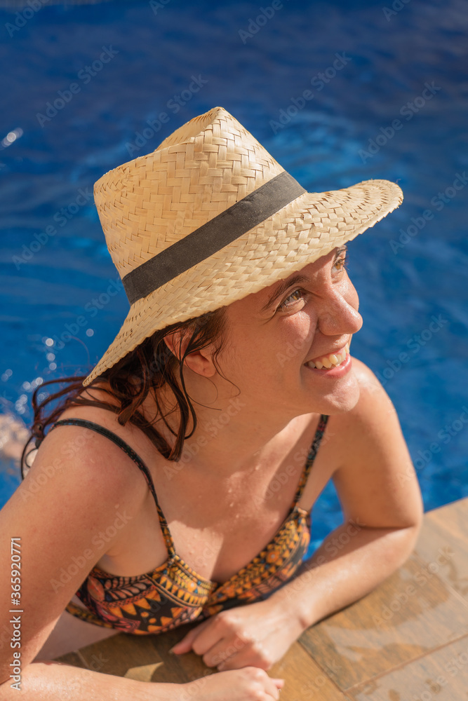 redhead pretty girl smiling wearing hat relaxing at the pool during summer holidays