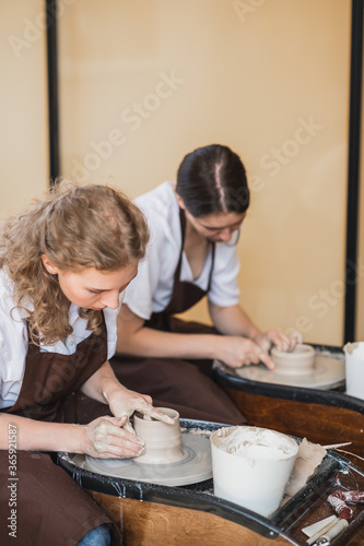 Two girls working on potters wheel making clay handmade craft in pottery workshop, friendship and guidance concept