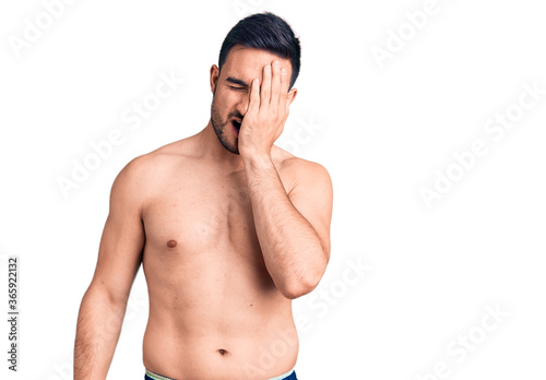 Young handsome man wearing swimwear yawning tired covering half face, eye and mouth with hand. face hurts in pain.