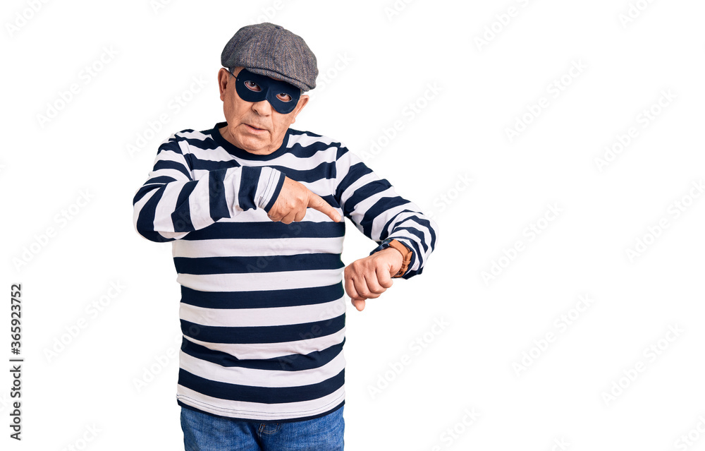 Senior handsome man wearing burglar mask and t-shirt in hurry pointing to watch time, impatience, upset and angry for deadline delay Senior handsome man wearing burglar mask and t-shirt in hurry pointing to watch time, impatience, upset and angry for deadline delay