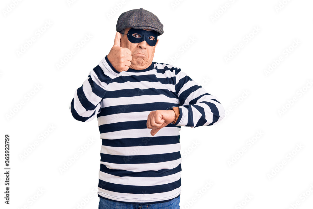 Senior handsome man wearing burglar mask and t-shirt doing thumbs up and down, disagreement and agreement expression. crazy conflict Senior handsome man wearing burglar mask and t-shirt doing thumbs up and down, disagreement and agreement expression. crazy conflict