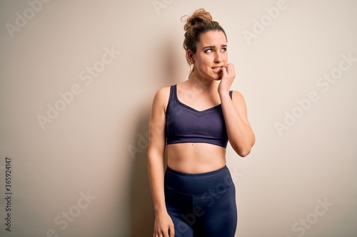 Young beautiful blonde sportswoman doing sport wearing sportswear over white background looking stressed and nervous with hands on mouth biting nails. Anxiety problem.