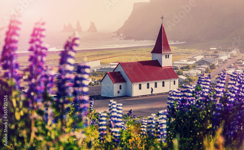 Colorfull misty morning view on Vik and Myrdal Church of Vikurkirkja with Reynisdrangar rock formations on background. Vik village is a one famous natural landmark and travel destination plase. © jenyateua