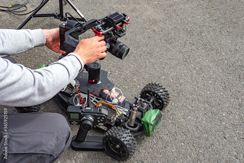 Man mounts a camera to a radio-controlled model of a car. Man sets a photo camera. Camera on the radio-controlled car. Man sets up photo equipment. Concept - professional filming equipment.