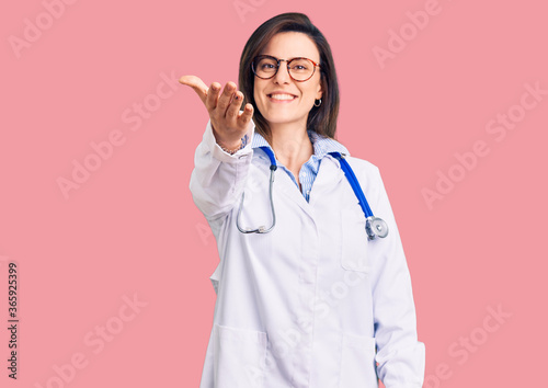 Young beautiful woman wearing doctor stethoscope and glasses smiling friendly offering handshake as greeting and welcoming. successful business.