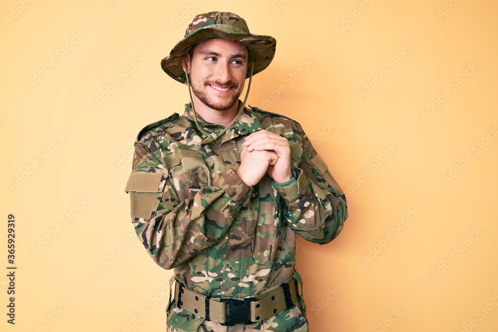 Fototapeta premium Young caucasian man wearing camouflage army uniform laughing nervous and excited with hands on chin looking to the side