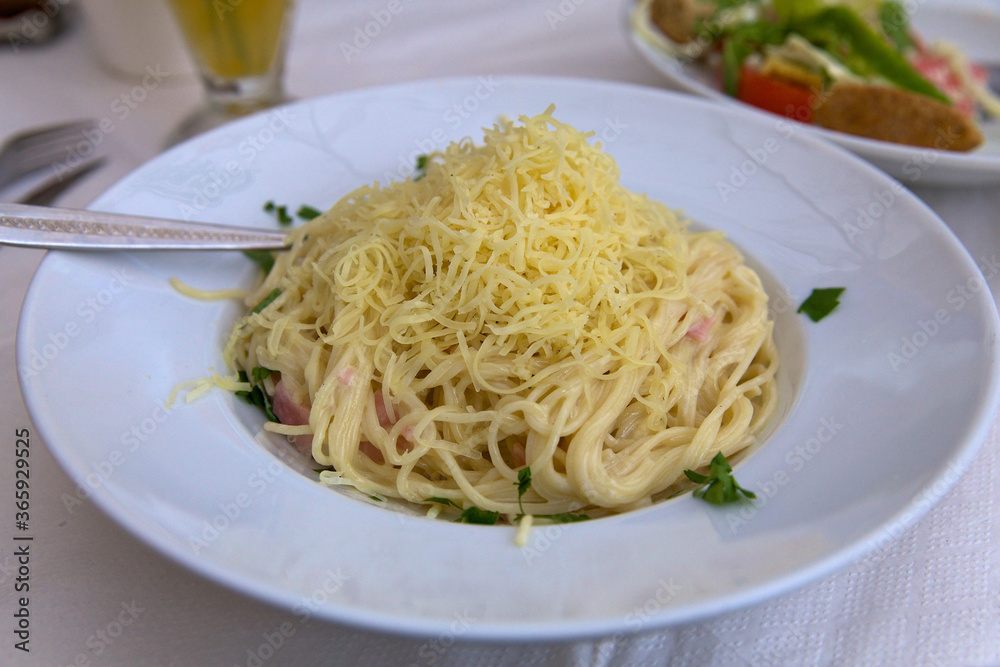 Close-up of food in a restaurant on the island of Crete. Carbonara pasta, sprinkled with grated cheese and garnished with herbs, on a large white plate