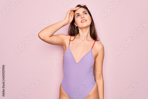 Young beautiful fashion girl wearing swimwear swimsuit and sunglasses over pink background smiling confident touching hair with hand up gesture  posing attractive and fashionable
