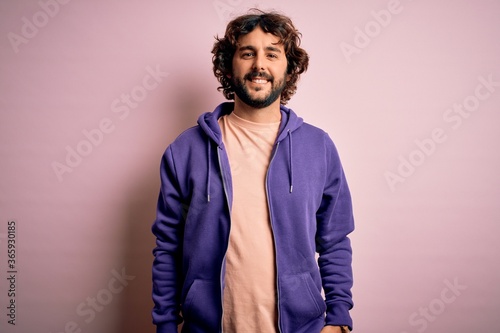 Young handsome sporty man with beard wearing casual sweatshirt over pink background with a happy and cool smile on face. Lucky person.