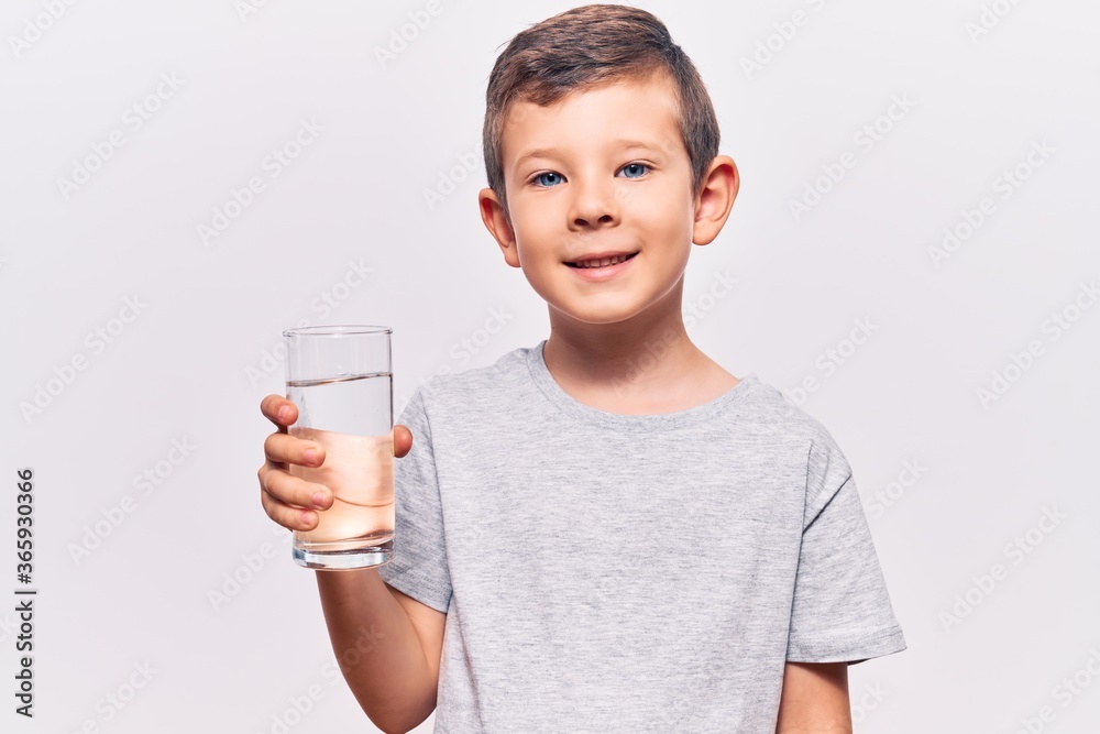 Cute blond kid drinking glass of water looking positive and happy standing and smiling with a confident smile showing teeth Cute blond kid drinking glass of water looking positive and happy standing and smiling with a confident smile showing teeth