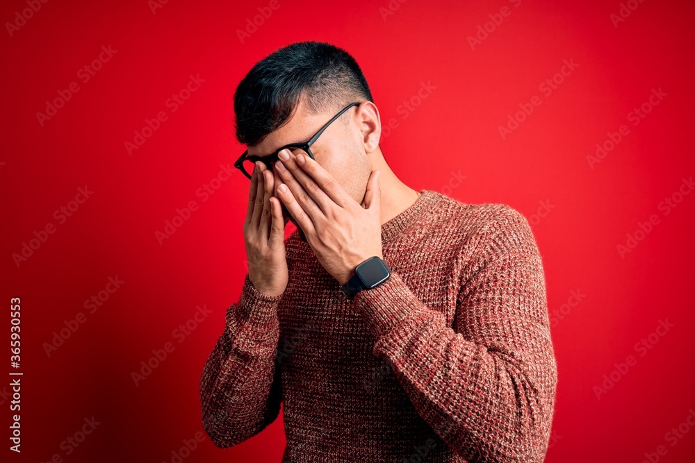 Young handsome hispanic man wearing nerd glasses over red background rubbing eyes for fatigue and headache, sleepy and tired expression. Vision problem Young handsome hispanic man wearing nerd glasses over red background rubbing eyes for fatigue and headache, sleepy and tired expression. Vision problem
