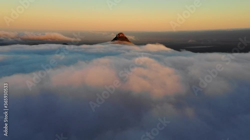 Aerial, drone shot rising over clouds towards a sunlit mountain peak, during sunset, in Hassell National Park, West Australia photo