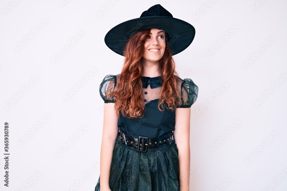 Young beautiful woman wearing witch halloween costume looking away to side with smile on face, natural expression. laughing confident. Young beautiful woman wearing witch halloween costume looking away to side with smile on face, natural expression. laughing confident.