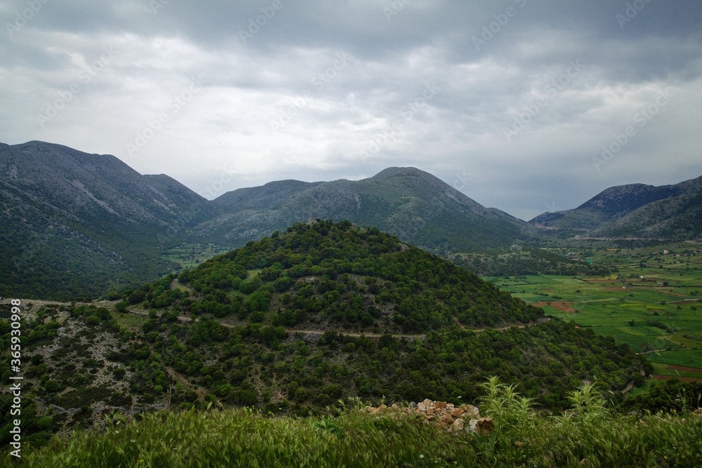 Natural landscape on the island of Crete in Greece, with views of a large green hill, meadows and mountains, in cloudy weather