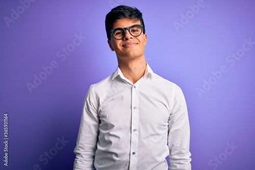 Young handsome business man wearing shirt and glasses over isolated purple background Relaxed with serious expression on face. Simple and natural looking at the camera.