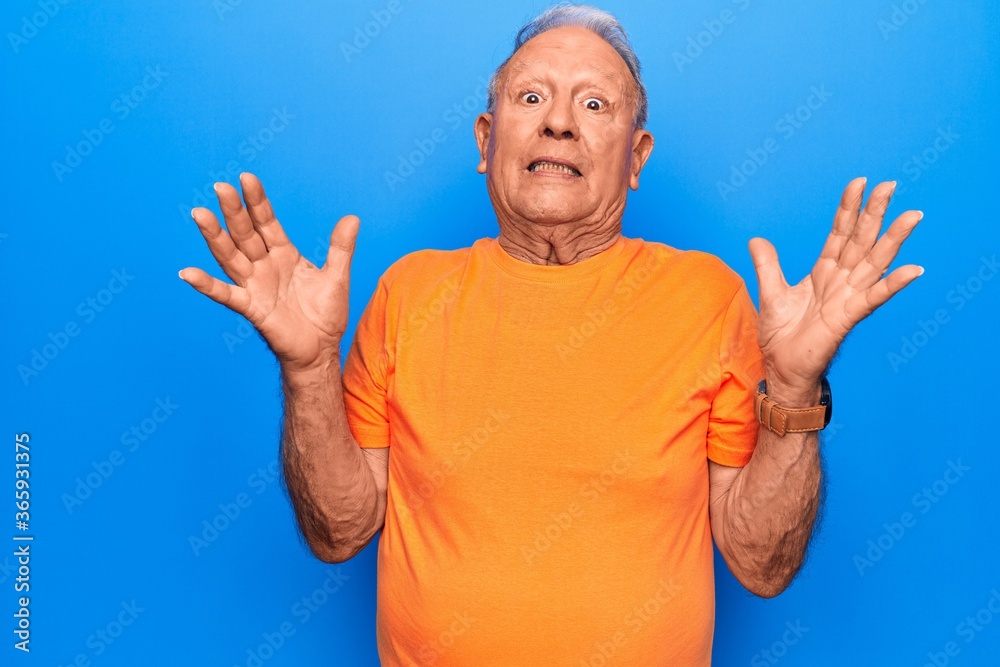 Senior handsome grey-haired man wearing casual t-shirt standing over blue background clueless and confused with open arms, no idea and doubtful face. Senior handsome grey-haired man wearing casual t-shirt standing over blue background clueless and confused with open arms, no idea and doubtful face.