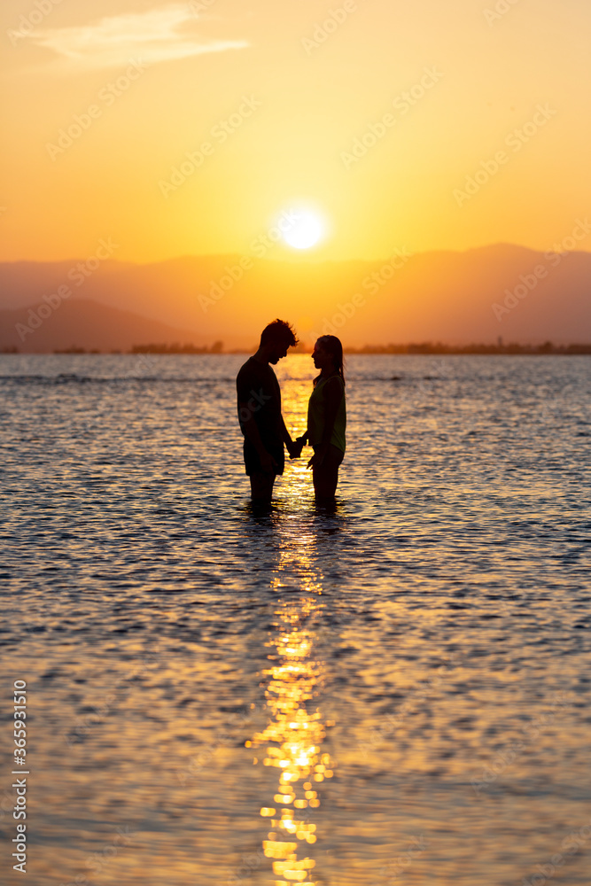 A young couple standing inside the water in the beach during the sunset