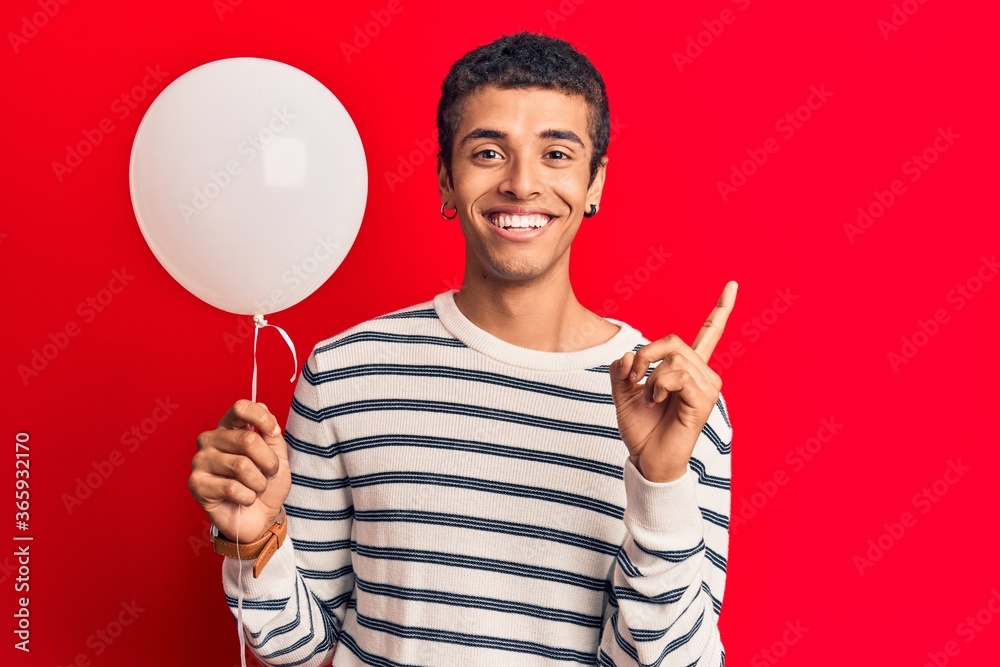 Young african amercian man holding balloon smiling happy pointing with hand and finger to the side Young african amercian man holding balloon smiling happy pointing with hand and finger to the side