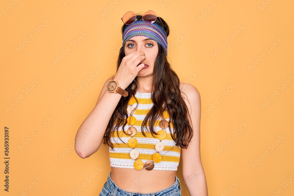 Young beautiful hippie woman with blue eyes wearing accesories and sunnglasses smelling something stinky and disgusting, intolerable smell, holding breath with fingers on nose. Bad smell Young beautiful hippie woman with blue eyes wearing accesories and sunnglasses smelling something stinky and disgusting, intolerable smell, holding breath with fingers on nose. Bad smell