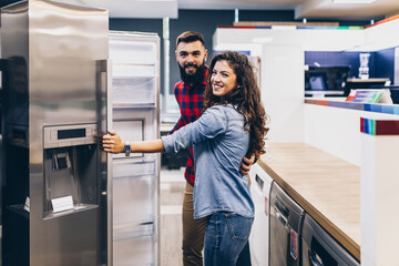 Young couple, satisfied customers choosing fridge in appliances store.