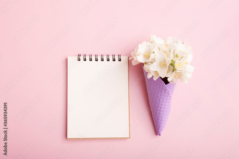 Blank notepad and flowers in a waffle cone on a pink background. Blank for congratulations, notes