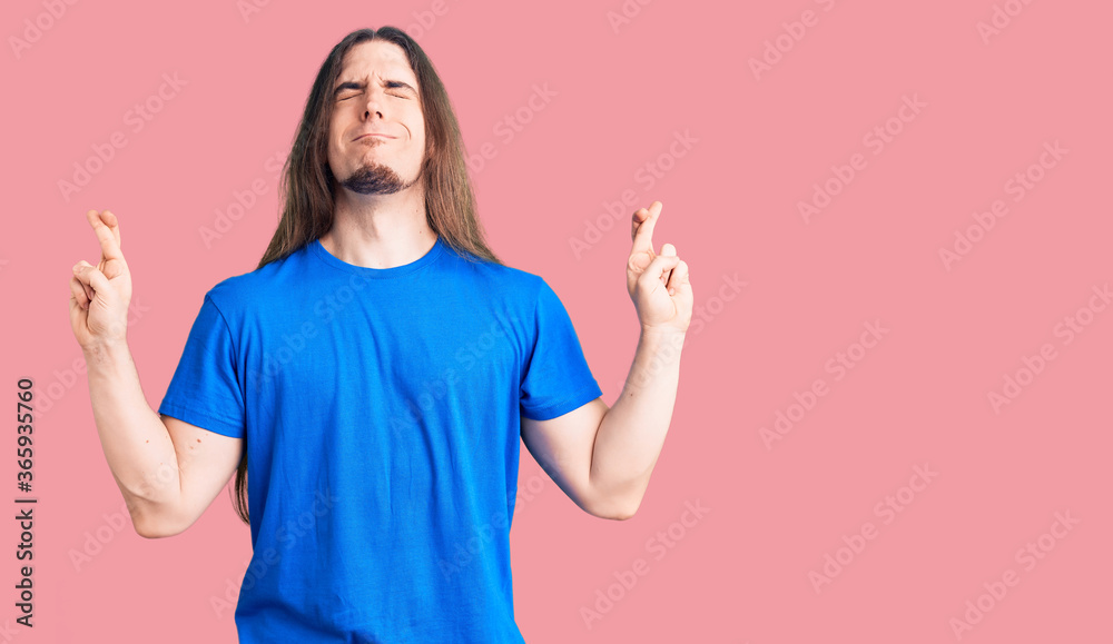 Young adult man with long hair wearing swimwear gesturing finger crossed smiling with hope and eyes closed. luck and superstitious concept. Young adult man with long hair wearing swimwear gesturing finger crossed smiling with hope and eyes closed. luck and superstitious concept.