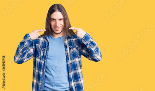 Young adult man with long hair wearing casual shirt smiling cheerful showing and pointing with fingers teeth and mouth. dental health concept. © Krakenimages.com