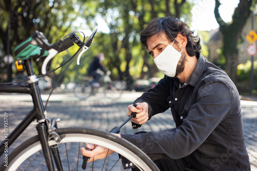 Man with face mask inflating the wheel of his bicycle on the street.