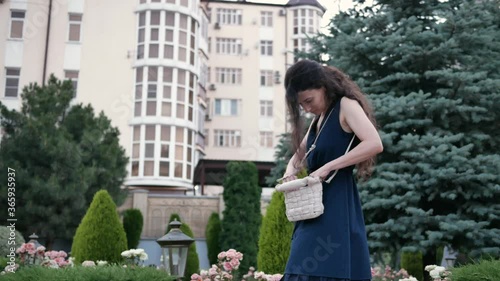 young beautiful woman on street in town in summer looking for your keys, lipstick or something in handbag outdoors