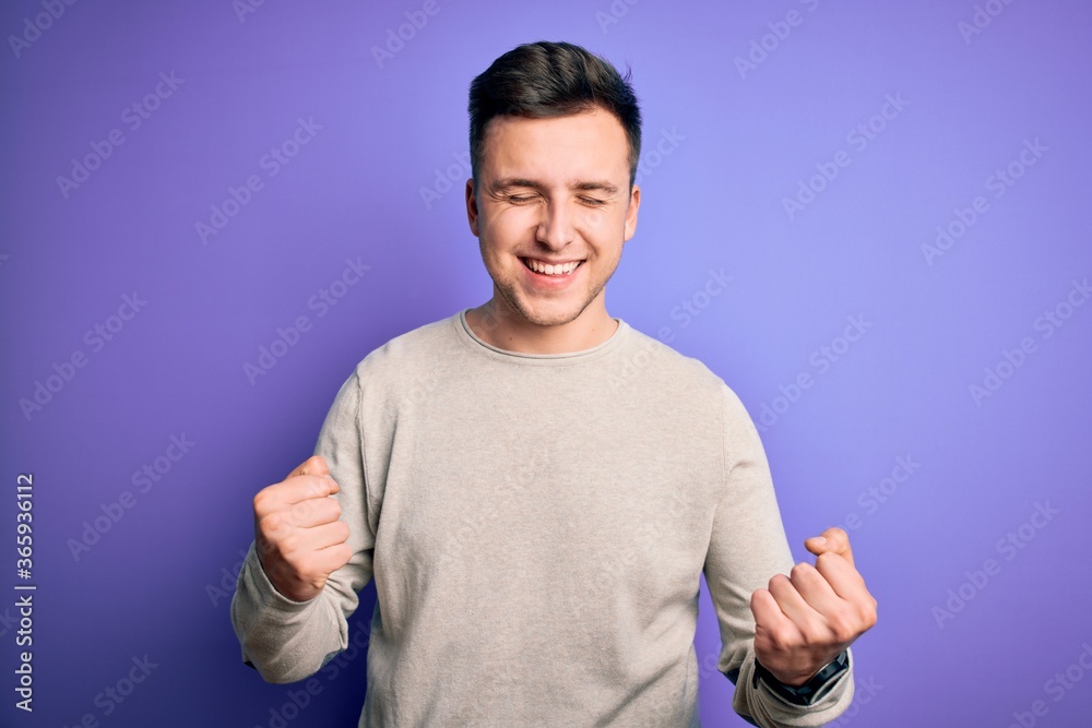Young handsome caucasian man wearing casual sweater over purple isolated background very happy and excited doing winner gesture with arms raised, smiling and screaming for success. Celebration Young handsome caucasian man wearing casual sweater over purple isolated background very happy and excited doing winner gesture with arms raised, smiling and screaming for success. Celebration
