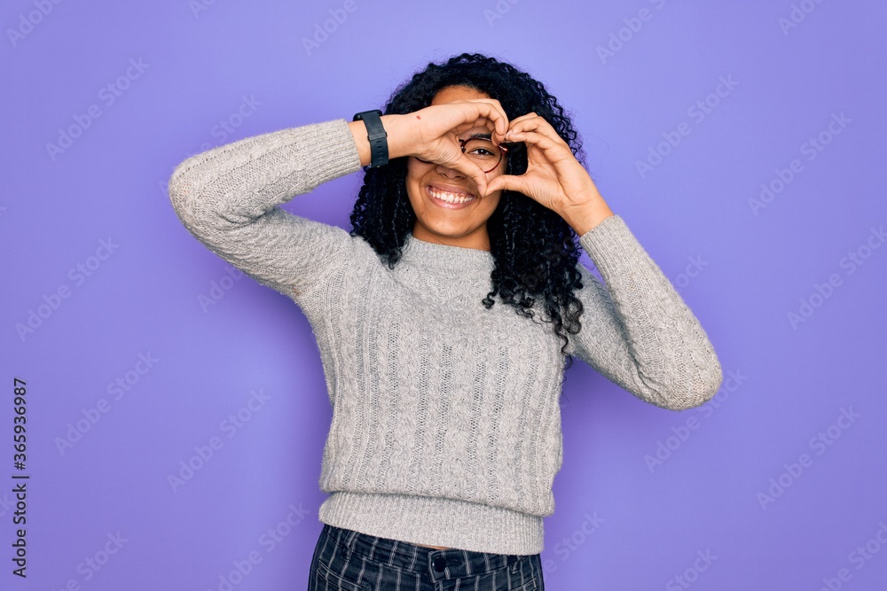 Young african american woman wearing casual sweater and glasses over purple background Doing heart shape with hand and fingers smiling looking through sign Young african american woman wearing casual sweater and glasses over purple background Doing heart shape with hand and fingers smiling looking through sign