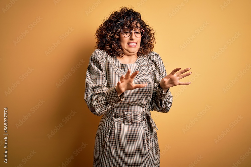 Beautiful arab business woman wearing dress and glasses standing over yellow background disgusted expression, displeased and fearful doing disgust face because aversion reaction. Beautiful arab business woman wearing dress and glasses standing over yellow background disgusted expression, displeased and fearful doing disgust face because aversion reaction.