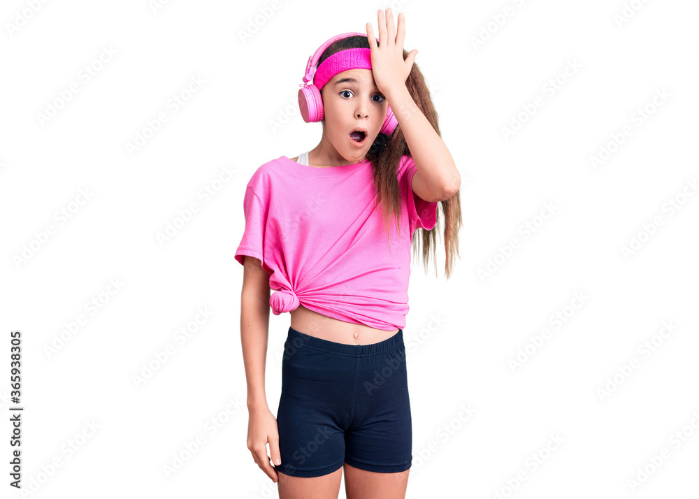 Cute hispanic child girl wearing gym clothes and using headphones surprised with hand on head for mistake, remember error. forgot, bad memory concept. Cute hispanic child girl wearing gym clothes and using headphones surprised with hand on head for mistake, remember error. forgot, bad memory concept.