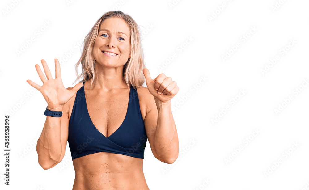 Middle age fit blonde woman wearing bikini showing and pointing up with fingers number six while smiling confident and happy. Middle age fit blonde woman wearing bikini showing and pointing up with fingers number six while smiling confident and happy.