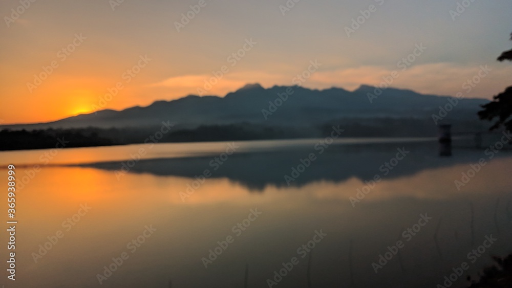 Landscape silhouette of mountains from the edge of the reservoir when the sun sets.