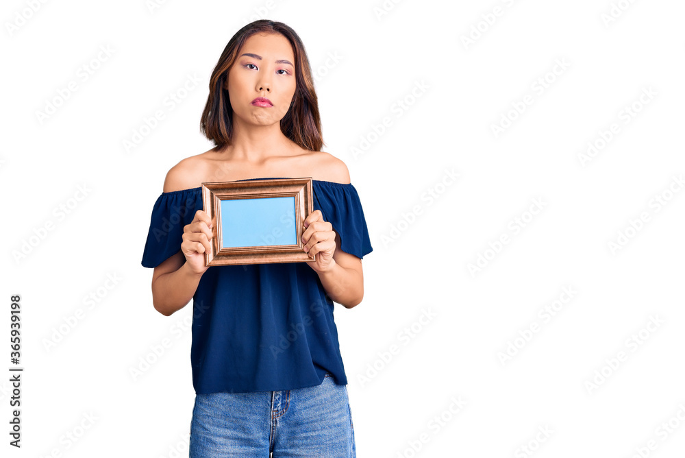 Young beautiful chinese girl holding empty frame thinking attitude and sober expression looking self confident Young beautiful chinese girl holding empty frame thinking attitude and sober expression looking self confident