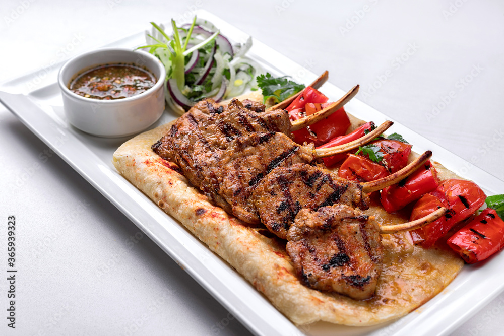 Pork, lamb ribs on pita bread, with baked bell pepper and sauce, on a white plate