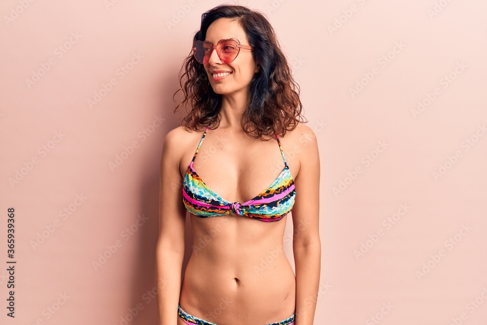Fototapeta premium Young beautiful hispanic woman wearing bikini and heart sunglasses looking to side, relax profile pose with natural face and confident smile.