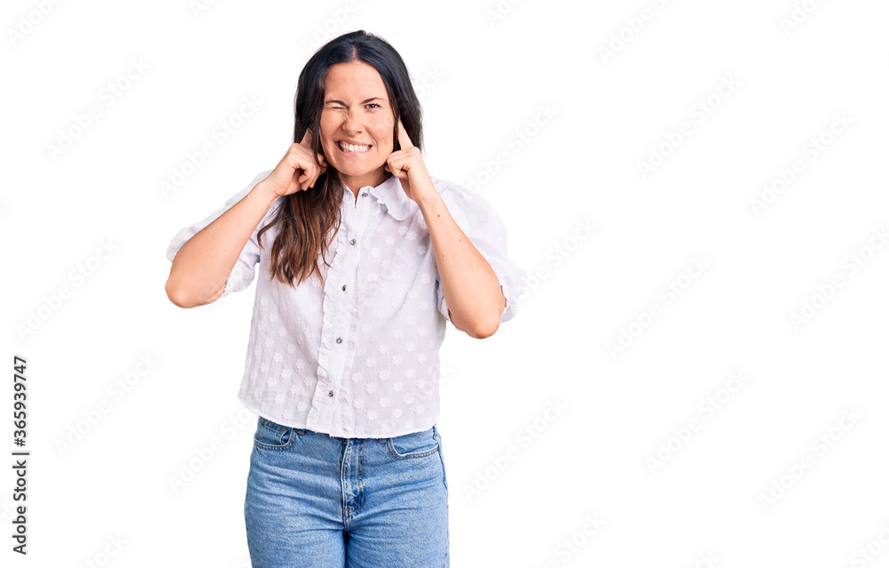 Young beautiful brunette woman wearing casual shirt covering ears with fingers with annoyed expression for the noise of loud music. deaf concept. Young beautiful brunette woman wearing casual shirt covering ears with fingers with annoyed expression for the noise of loud music. deaf concept.