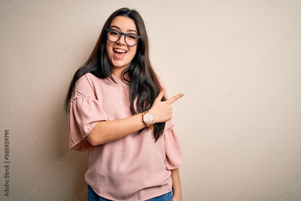 Young brunette elegant woman wearing glasses over isolated background cheerful with a smile of face pointing with hand and finger up to the side with happy and natural expression on face Young brunette elegant woman wearing glasses over isolated background cheerful with a smile of face pointing with hand and finger up to the side with happy and natural expression on face