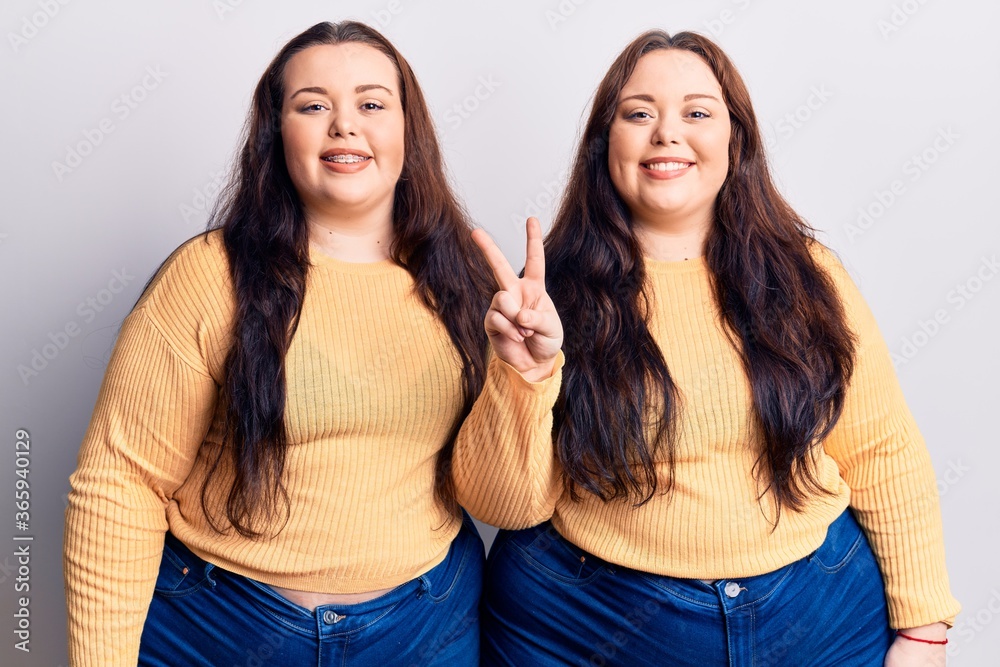Young plus size twins wearing casual clothes showing and pointing up with fingers number two while smiling confident and happy. Young plus size twins wearing casual clothes showing and pointing up with fingers number two while smiling confident and happy.