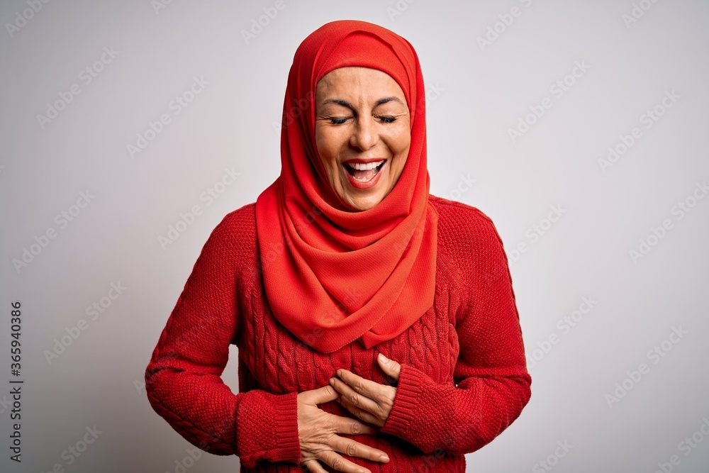 Middle age brunette woman wearing muslim traditional hijab over isolated white background smiling and laughing hard out loud because funny crazy joke with hands on body. Middle age brunette woman wearing muslim traditional hijab over isolated white background smiling and laughing hard out loud because funny crazy joke with hands on body.