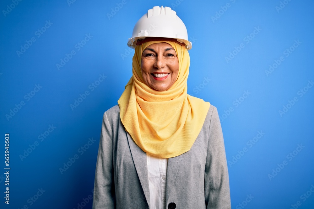 Middle age brunette architect woman wearing muslim traditional hijab and security helmet with a happy and cool smile on face. Lucky person.